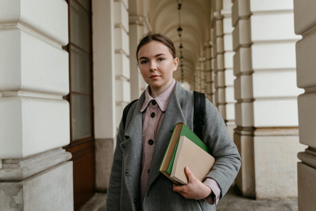 Young woman holding books in a corridor with arches.