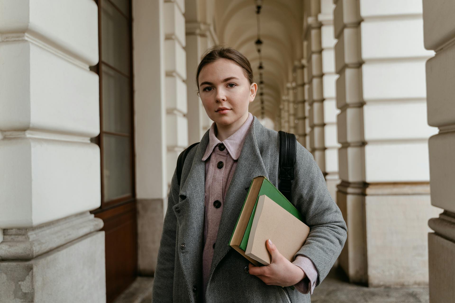 Young woman holding books in a corridor with arches.