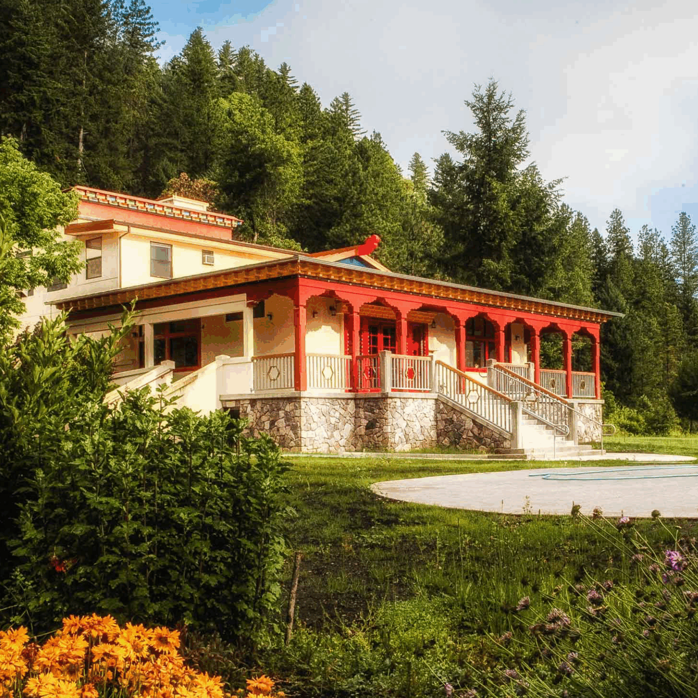 A charming house with red accents surrounded by greenery and flowers.
