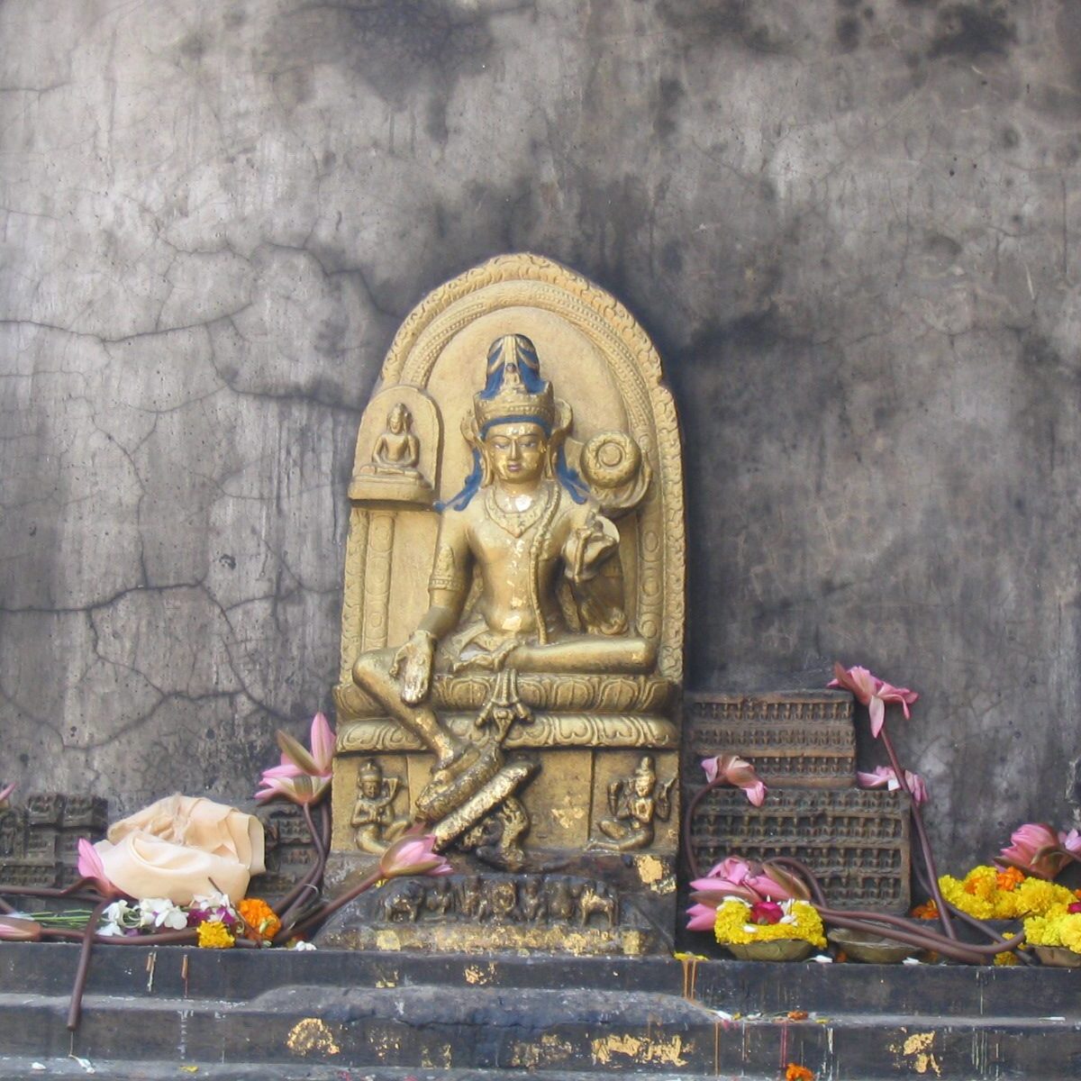 Golden Hindu deity statue adorned with flowers against a stone wall.