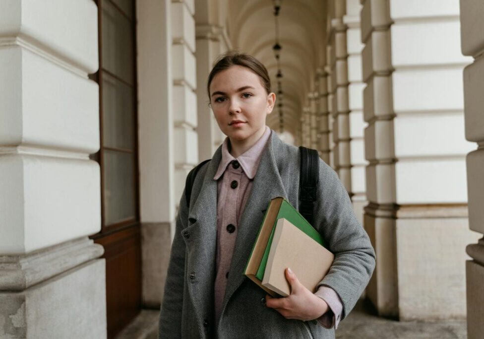 Young woman holding books in a corridor with arches.